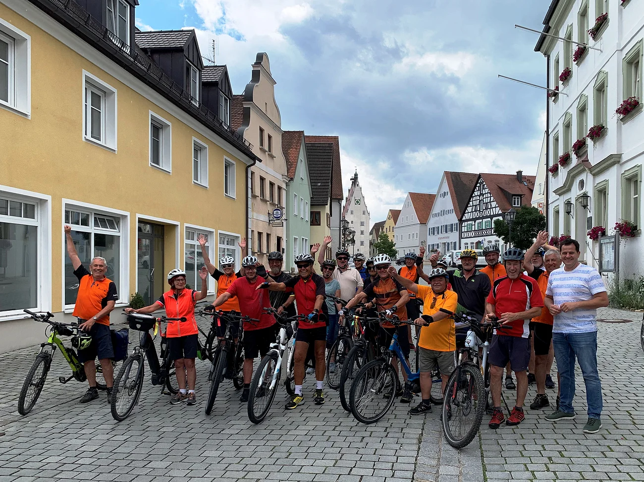 Gruppe von Radfahrern in bunter Sportkleidung posiert mit Fahrrädern auf einer gepflasterten Straße in einer Stadt.