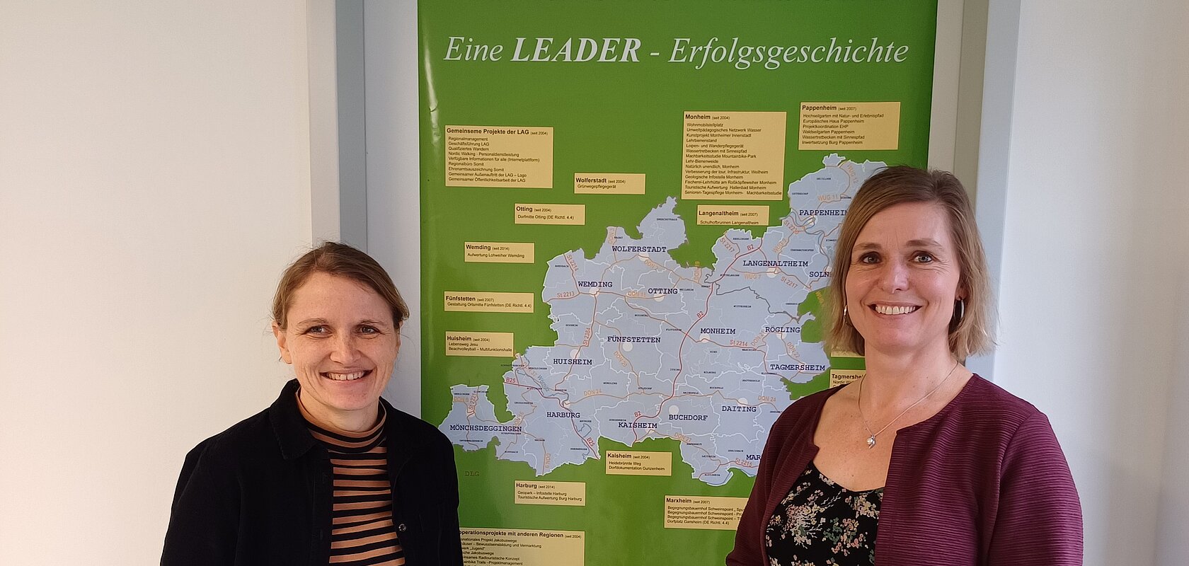 Zwei lächelnde Personen stehen vor einem grünen Plakat mit einer Karte der Region Monheimer Alb-AltmühlJura. Umgeben von einer weißen Wand.