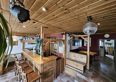 Monheimer Nest - Theke Ein rustikaler Barbereich mit Holzmöbeln, einer Theke, Barhockern, einem schwarzen Scheinwerfer und einer Discokugel an der Decke.