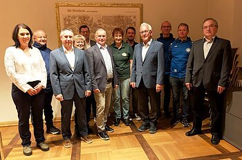 Elf Personen stehen in einem Raum vor einer alten Landkarte an der Wand, teils in Anzügen, teils in Freizeitkleidung. Spendenübergabe der Sparkasse Nordschwaben an Monheimer Vereine und Verbände.