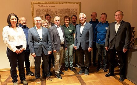 Elf Personen stehen in einem Raum vor einer alten Landkarte an der Wand, teils in Anzügen, teils in Freizeitkleidung. Spendenübergabe der Sparkasse Nordschwaben an Monheimer Vereine und Verbände.