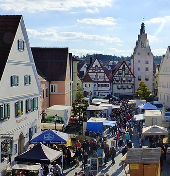 Menschenmenge auf dem belebten Monheimer Marktplatz mit historischen Gebäuden und vielen Verkaufsständen bei sonnigem Wetter.