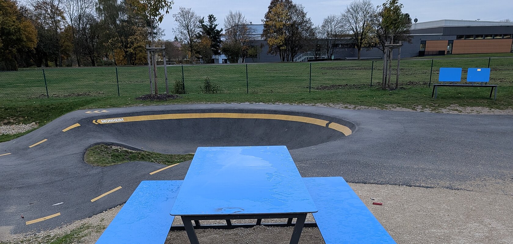 Blauer Picknicktisch mit Bänken auf Kiesfläche, davor verstreute rote Feuerwerkskörperreste. Verschmutzung an der Pumptrack-Anlage in Monheim.