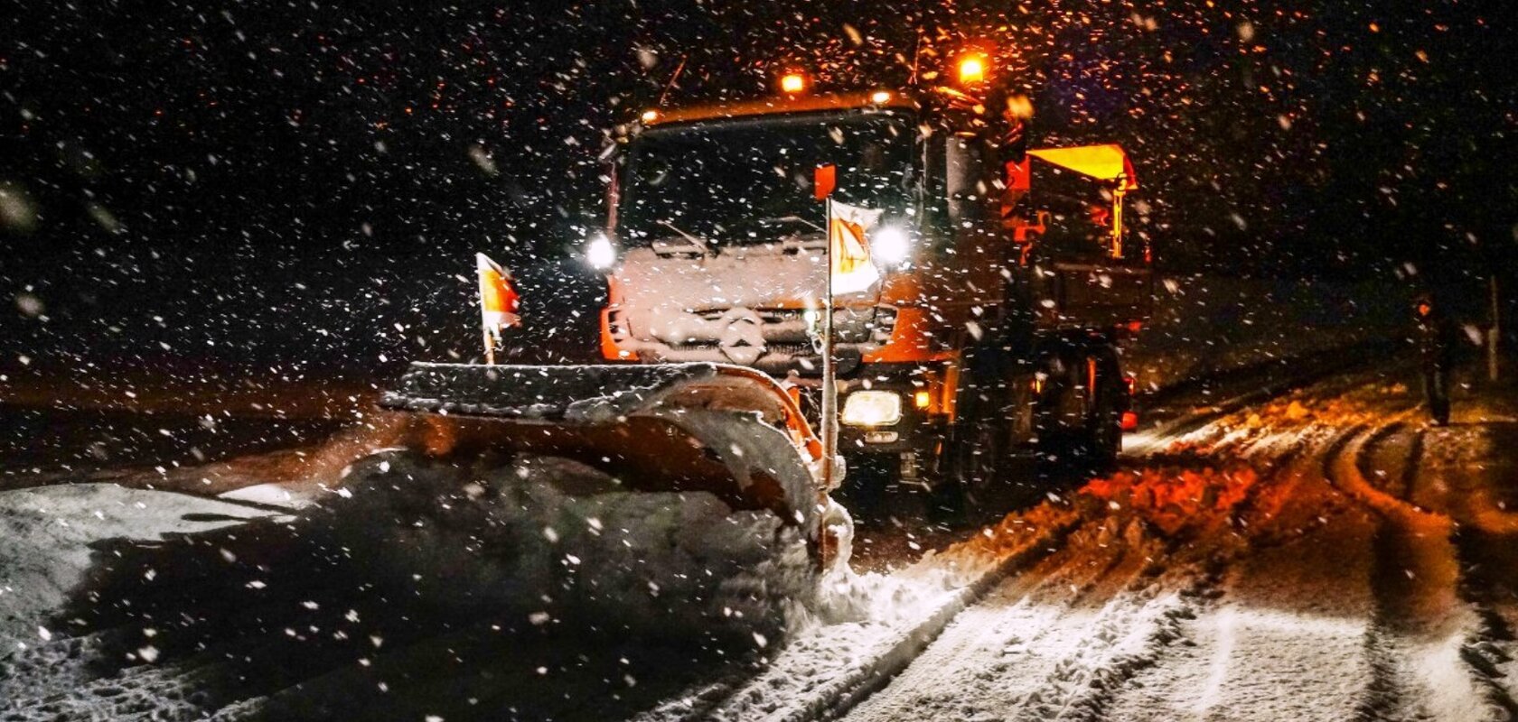 Ein Schneepflug räumt nachts eine verschneite Straße, während es schneit.