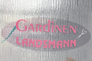 Aufgeklebtes Logo mit Schriftzug „Gardinen Landsmann“ in pink hinter einer strukturierten Glasfläche mit silberner Schere rechts neben dem Schriftzug und einem Zickzack-Motiv in türkis links neben dem Schriftzug.