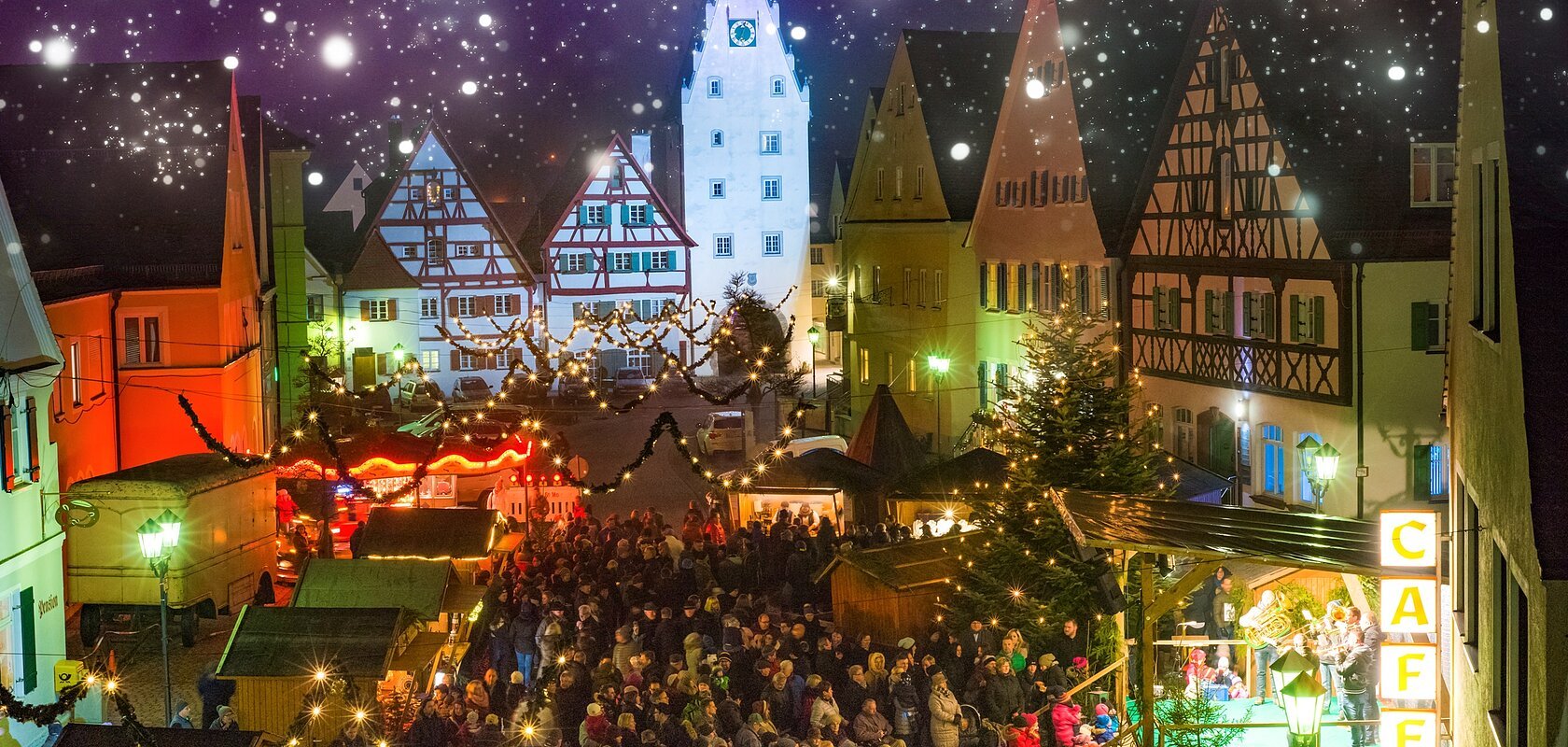Abendaufnahme des belebten Monheimer Weihnachtsmarktes in der Altstadt von Monheim: mit Fachwerkhäusern, Menschenmengen, Lichtern, Verkaufsständen und einer Bühne.