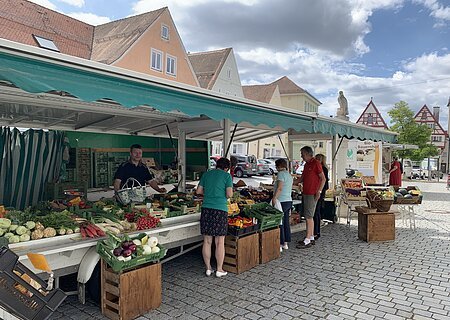 Wochenmarkt Monheim Marktstand des Wochenmarkts in Monheim mit Obst und Gemüse in der Auslage auf dem gepflastertem Marktplatz. Mehrere Personen kaufen dort ein. Fachwerkhäuser im Hintergrund und bewölkter Himmel.