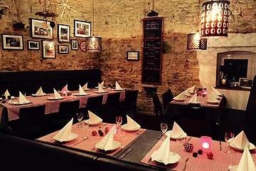 Gemütliches Restaurant mit Tischen, die mit weißen Servietten, Gläsern und roten Tischläufern in einem Raum mit Steinwänden gedeckt sind. Bilderrahmen hängen an den Wänden