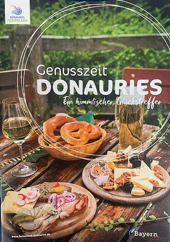 Brotzeit mit Brezeln, Käse, Wurst, Wein und Bier auf Holztisch im Freien, Neuauflage 11/2025 der Broschüre Genusszeit vom Ferienland Donauries