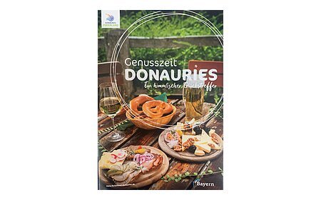 Brotzeit mit Brezeln, Käse, Wurst, Wein und Bier auf Holztisch im Freien, Neuauflage 11/2025 der Broschüre Genusszeit vom Ferienland Donauries