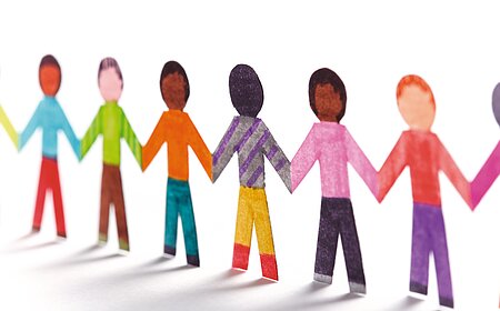 Papierfiguren, die Kinder symbolisieren in verschiedenen Farben halten sich an den Händen und bilden eine Kette.