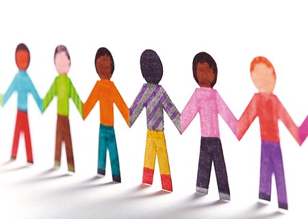 Papierfiguren, die Kinder symbolisieren in verschiedenen Farben halten sich an den Händen und bilden eine Kette.