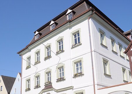 Das Rathaus der Stadt Monheim, am Marktplatz. Ein weißes, dreistöckiges Gebäude mit Satteldach und mehreren Fenstern, im Vordergrund gepflasterter Marktplatz.