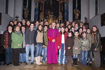 Gruppenfoto von 34 Personen in einer Kirche vor einem Altar mit goldenen Verzierungen und Kerzen im Hintergrund. Dunkler gemusterter Bodenbelag aus Fließen im Vordergrund.