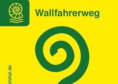 Leuchtend gelbes Wallfahrerweg-Schild: darauf mittig ein grünes Spiralsymbol mit Schrift „Wallfahrerweg“ oberhalb. Links daneben das Symbol eines Schneckenfossils. Vom unteren Eck links vertikal hoch die Nennung der Website "www.naturpark-altmuehltal.de"
