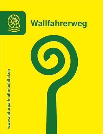 Leuchtend gelbes Wallfahrerweg-Schild: darauf mittig ein grünes Spiralsymbol mit Schrift „Wallfahrerweg“ oberhalb. Links daneben das Symbol eines Schneckenfossils. Vom unteren Eck links vertikal hoch die Nennung der Website "www.naturpark-altmuehltal.de"