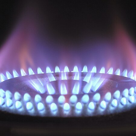 Blaue Gasflamme brennt rund um den Brenner eines Gasherds vor schwarzem Hintergrund.