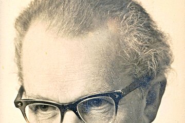 Porträt eines älteren Mannes mit Brille, Hemd und Sakko, Blick leicht nach unten gerichtet.