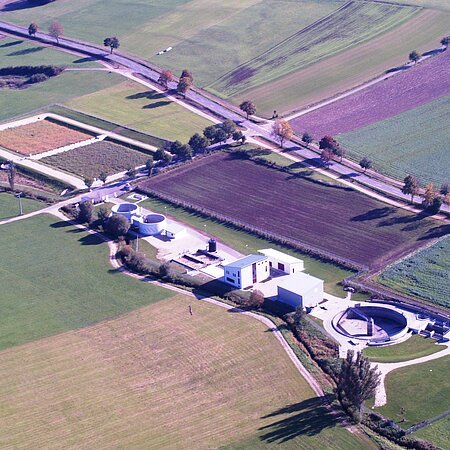 Luftaufnahme einer Kläranlage umgeben von Feldern und Straßen mit Bäumen entlang der Wege.