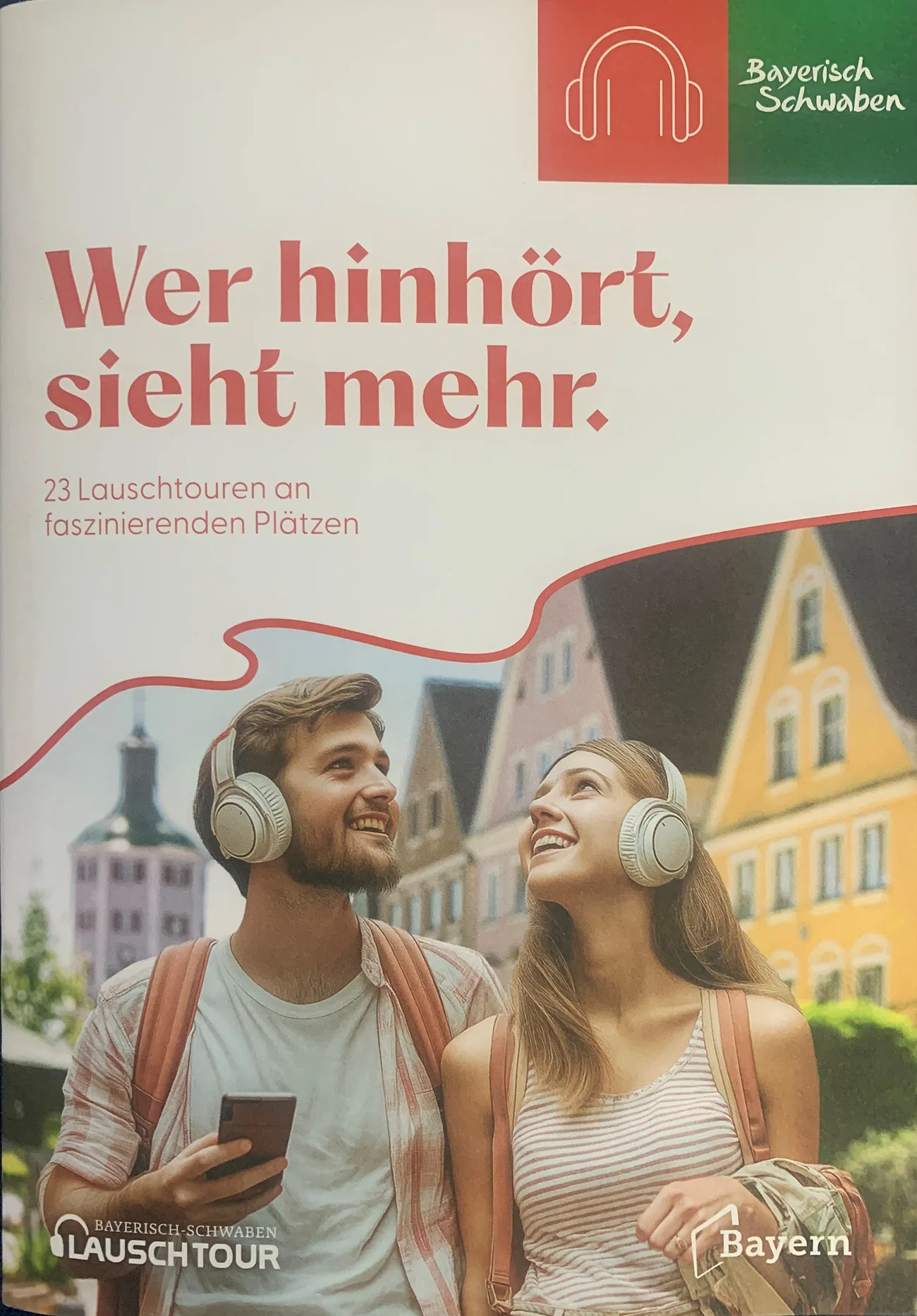 Broschüre Lauschtouren Allgäu/Bayerisch-Schwaben Titelblatt der Broschüre "Wer hinhört, sieht mehr" zu Lauschtouren vom Tourismusverband Allgäu/Bayerisch-Schwaben e.V.. Auf dem Foto zwei junge Personen mit hellen Kopfhörern und Rucksäcken vor bunten Häusern in einer Stadt in Bayern. Auf dem Foto der Text "23 Lauschtouren an faszinierenden Plätzen".