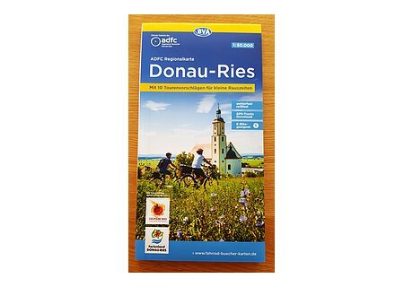 Cover der ADFC Regionalkarte Donau-Ries mit Radfahrern vor Kirche und Landschaft im Hintergrund. Unten links im Bild Logos vom Ferienland Donauries und des Geopark Ries.