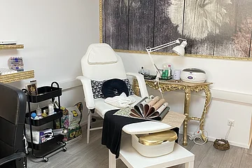 Behandlungsraum mit weißem Stuhl, Rollwagen, goldfarbenem Tisch und großem Blumenbild an der Wand.