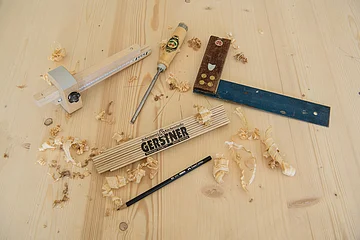 Holzwerkzeuge, Bleistift und Zollstock auf Holzplatte mit Holzspänen verteilt.