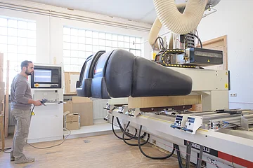 Mann bedient große CNC-Holzbearbeitungsmaschine in heller Werkstatt mit Steuergerät in der Hand.