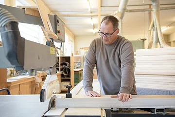Mann mit Brille bedient eine Tischkreissäge in einer hellen Holzwerkstatt.