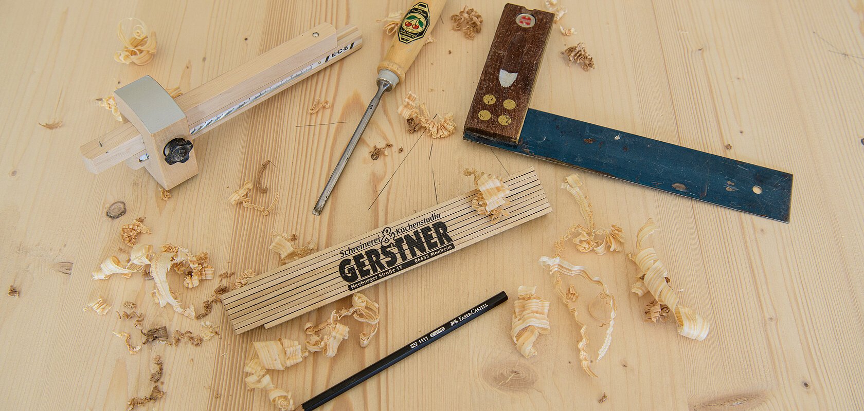 Holzwerkzeuge, Bleistift und Zollstock auf Holzplatte mit Holzspänen verteilt.