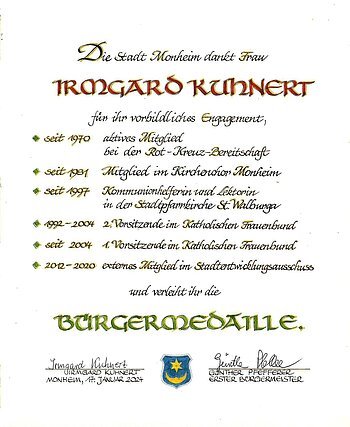 Urkunde der Stadt Monheim für Irmgard Kuhnert mit Aufzählung der Tätigkeiten zu ihrem vorbildlichen Engagement und zur Verleihung der Bürgermedaille, darunter zwei Unterschriften und ein Wappen der Stadt Monheim. Datiert 17. Januar 2024.