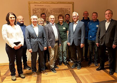 Elf Personen stehen in einem Raum vor einer alten Landkarte an der Wand, teils in Anzügen, teils in Freizeitkleidung. Spendenübergabe der Sparkasse Nordschwaben an Monheimer Vereine und Verbände.