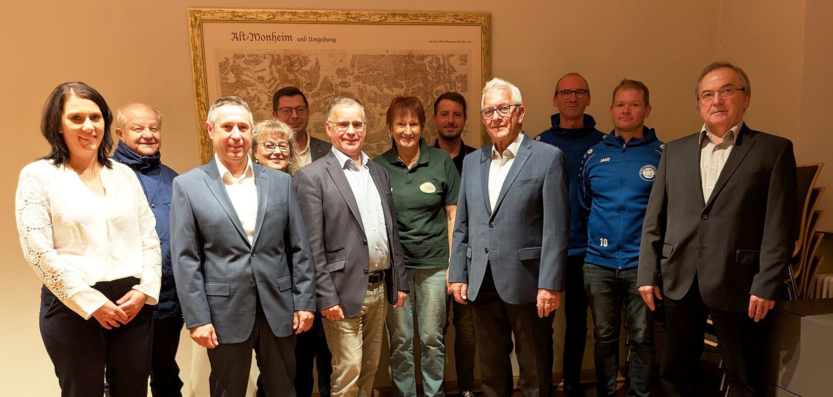 Elf Personen stehen in einem Raum vor einer alten Landkarte an der Wand, teils in Anzügen, teils in Freizeitkleidung. Spendenübergabe der Sparkasse Nordschwaben an Monheimer Vereine und Verbände.
