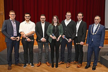 Sieben Personen stehen nebeneinander vor rotem Vorhang, sechs halten Auszeichnungen, eine trägt eine Amtskette. Ehrung am Neujahrsempfang 2026 der Stadt Monheim - Schützengesellschaft Monnheim mit dem Stadtmeister.