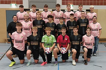 Mannschaftsfoto einer Fußballjugend in Sportkleidung in einer Sporthalle, 21 Personen in drei Reihen, zwei Spieler in der Mitte halten Bälle.