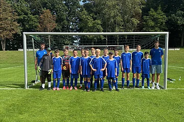 Jugendfußballmannschaft mit Trainern steht vor dem Tor auf dem grünem Spielfeld im Freien bei Tageslicht.