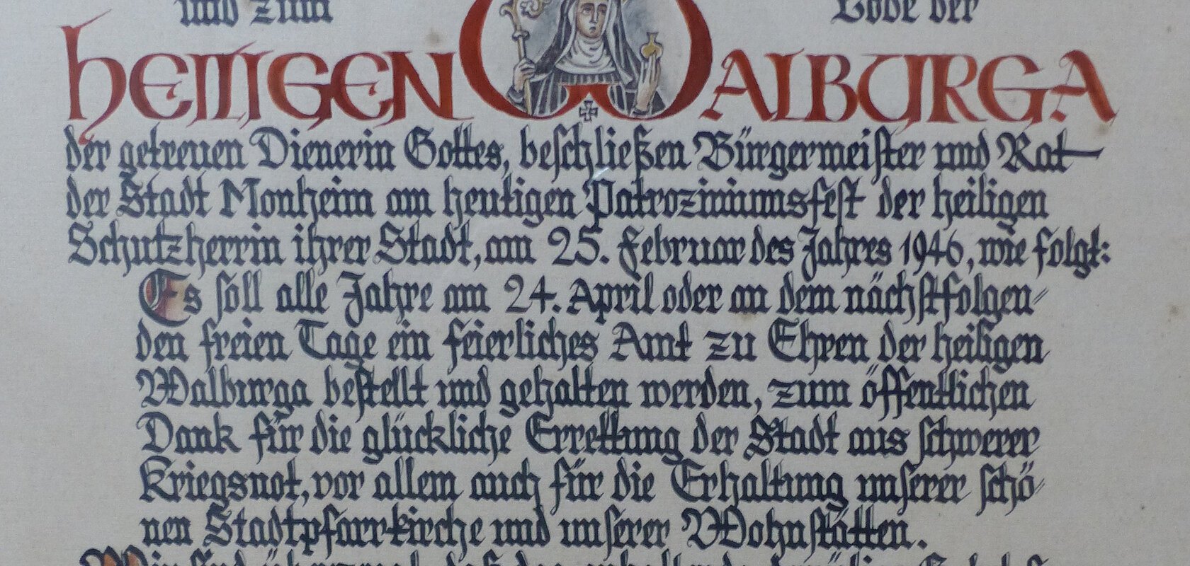Ein handgeschriebenes Dokument mit dekorativen roten und schwarzen Buchstaben, das eine religiöse Widmung enthält. Hierin gelobt der Bürgermeister sowie der Rat der Stadt Monheim, ein alljährliches Dankamt zu Ehren der Heiligen Walburga abhalten zu lassen, für die Verschonung der Stadt im Zweiten Weltkrieg.
