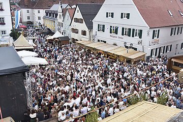 Große Menschenmenge auf dem historischen Stadtfest in der Altstadt von Monheim, mit Ständen und historischen Gebäuden im Hintergrund. Eine blau/weiße Flagge hängt an einem Gebäude.