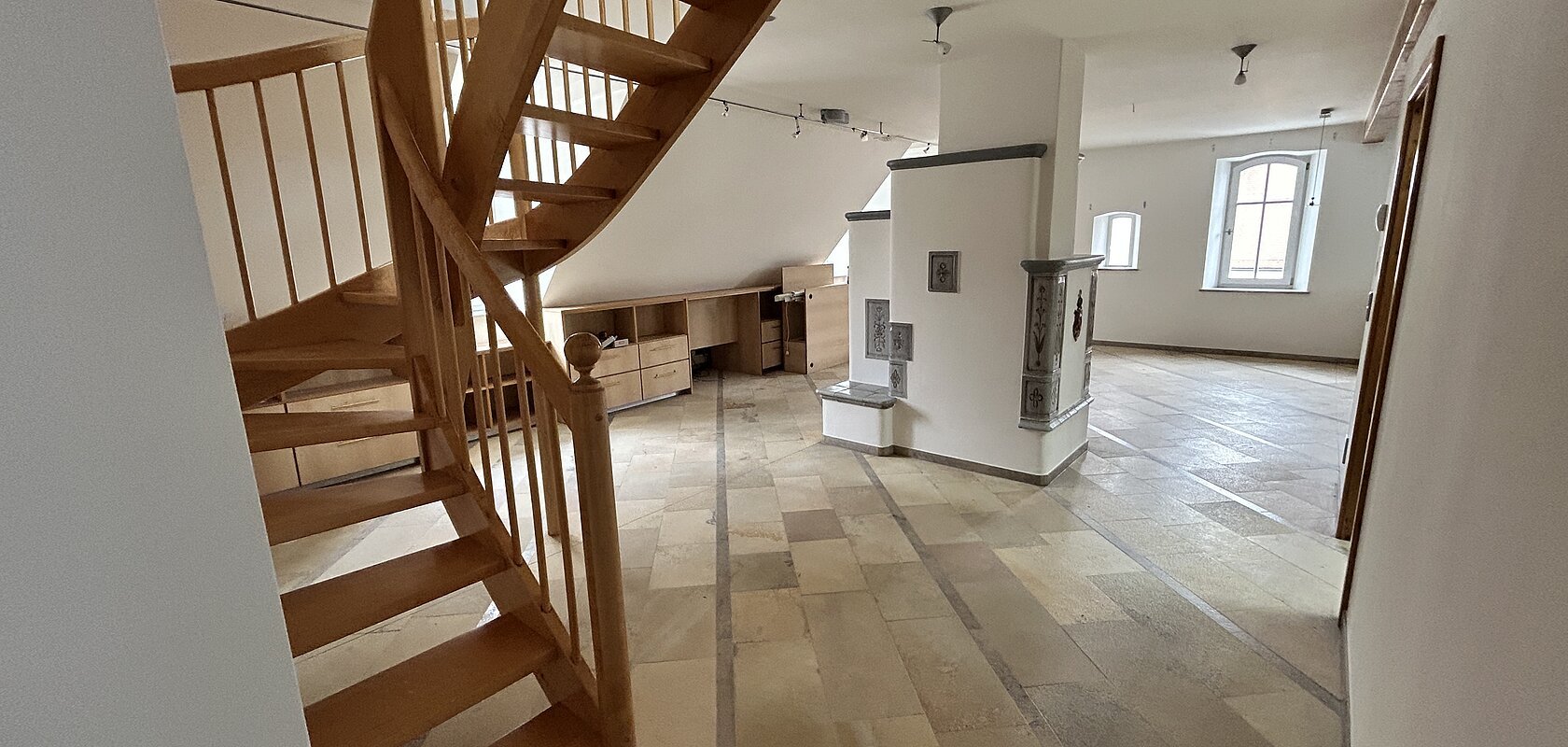 Mietobjekt Maisonetten Wohnung Marktplatz 11, Monheim.
Offener Raum mit Holztreppe, Fliesenboden, weißen Wänden und zwei Fenstern in einer Dachgeschosswohnung