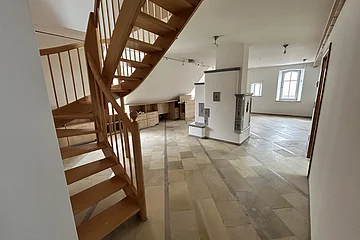 Mietobjekt Maisonetten Wohnung Marktplatz 11, Monheim.
Offener Raum mit Holztreppe, Fliesenboden, weißen Wänden und zwei Fenstern in einer Dachgeschosswohnung