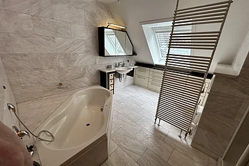 Miet-Maisonette. Badezimmer mit Badewanne, Waschbecken, Spiegelschrank, Dachfenster und Heizkörper vor Fliesenwand und -boden.