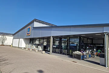 Außenansicht eines Aldi Süd Supermarkts bei sonnigem Wetter umgeben von einem Parkplatz.