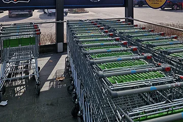 Überdachter Einkaufswagenbereich aus Glas mit Aldi-Werbung darin und geparkten Autos im Hintergrund.