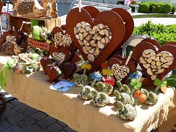Marktstand mit Holzherzen, Holztieren und dekorativen Figuren aus Stroh auf einem mit Leinen bedeckten Tisch.
