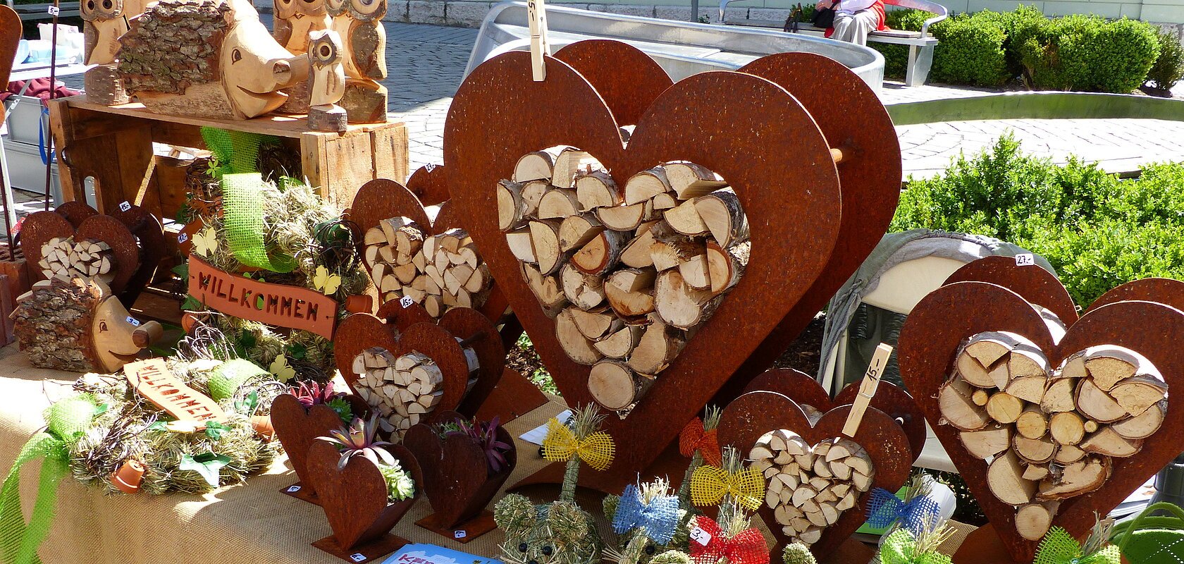 Marktstand mit Holzherzen, Holztieren und dekorativen Figuren aus Stroh auf einem mit Leinen bedeckten Tisch.