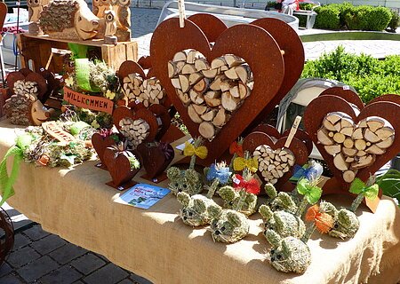 Marktstand mit Holzherzen, Holztieren und dekorativen Figuren aus Stroh auf einem mit Leinen bedeckten Tisch.