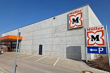 Außenansicht eines Müller-Marktes mit Parkplätzen und blauem Himmel.