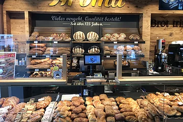 Bäckerei-Theke mit einer Vielzahl von Broten und Backwaren hinten auf Regalen und in Auslagen. An der Wand gelbe Aufschrift "Aroma".