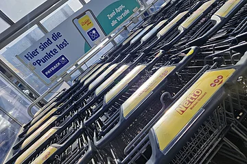 Eingeschobene Einkaufswagen mit Netto-Logo vor Werbetafel für PAYBACK-Punkte und zwei Apps.