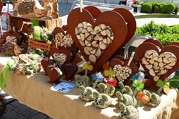 Marktstand mit Holzherzen, Holztieren und dekorativen Figuren aus Stroh auf einem mit Leinen bedeckten Tisch.